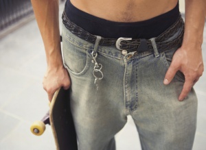 Man holding skateboard with key hooked on belt loop