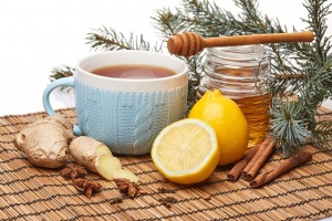 Honey in glass pot and blue cup of tea with ginger, cinnamon, anise and lemon standing on bamboo mat on a white background.